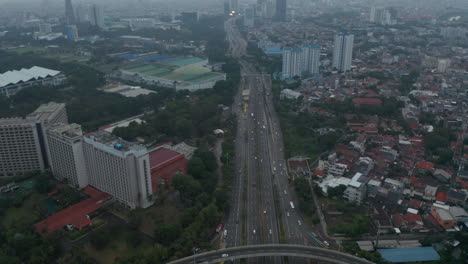 Aerial-dolly-tilt-shot-following-cars-on-a-multi-lane-highway-and-revealing-wide-view-of-modern-urban-city-skyline-of-Jakarta,-Indonesia