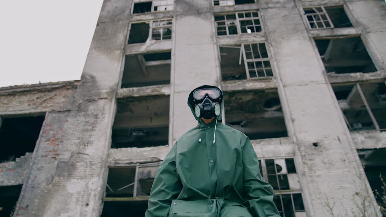 Portrait of a man in safety suit in radiation zone. Person in gas mask and protective uniform standing alone on ruined building background. Apocalypse concept.