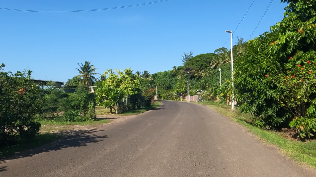 Bora Bora, French Polynesia. Moving on Asphalt Road Around Island, Tropical Lush and Buildings Point of View