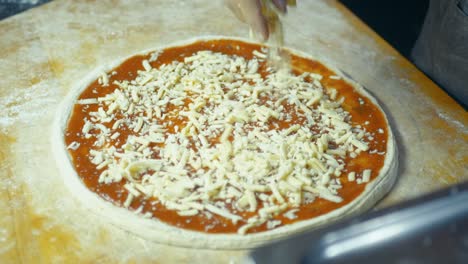 closeup of chef adding cheese to pizza dough topped with tomato sauce in handmade pizza preparation.