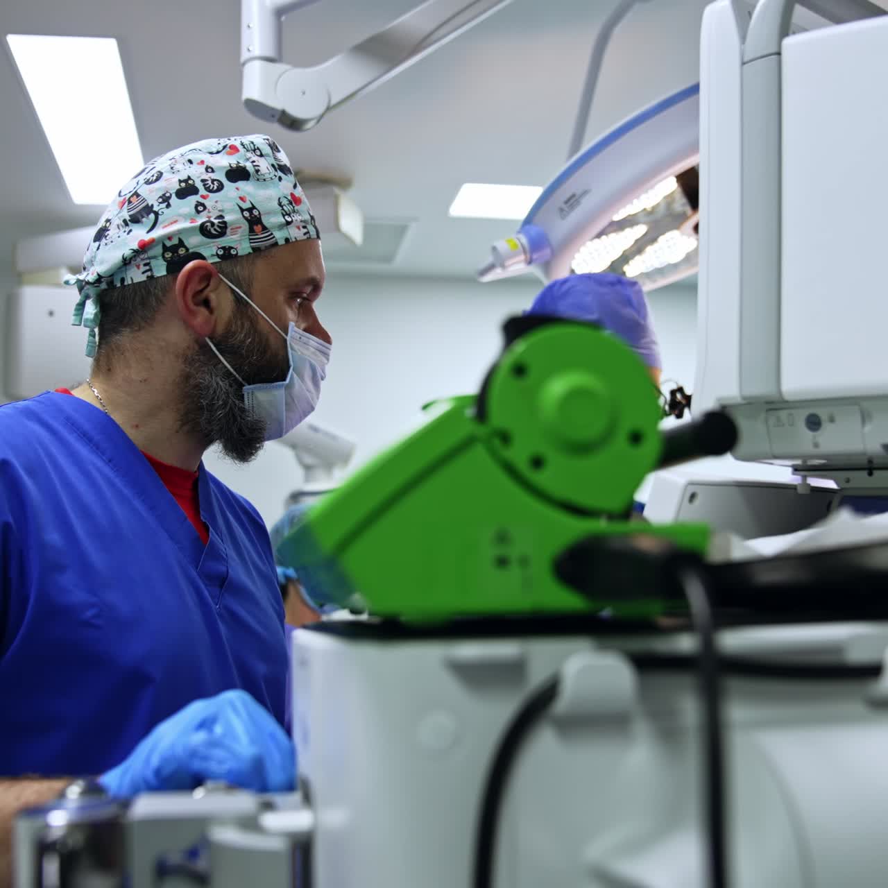 Large experienced team of medics working in the surgery room at operation. Male anesthesiologist stands at monitors of lung ventilator checking the patient's condition