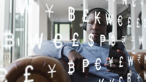 animation of currency symbols over african american man using smartphone