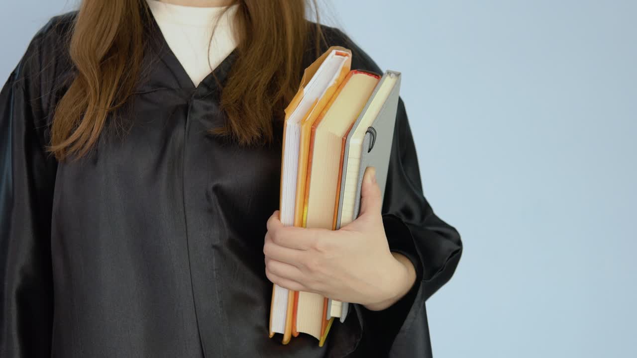 검은 옷을 입은 여학생의 손에 수직 위치에 있는 여러 교과서, 색 배경에 가까운 책과 손의 시각.