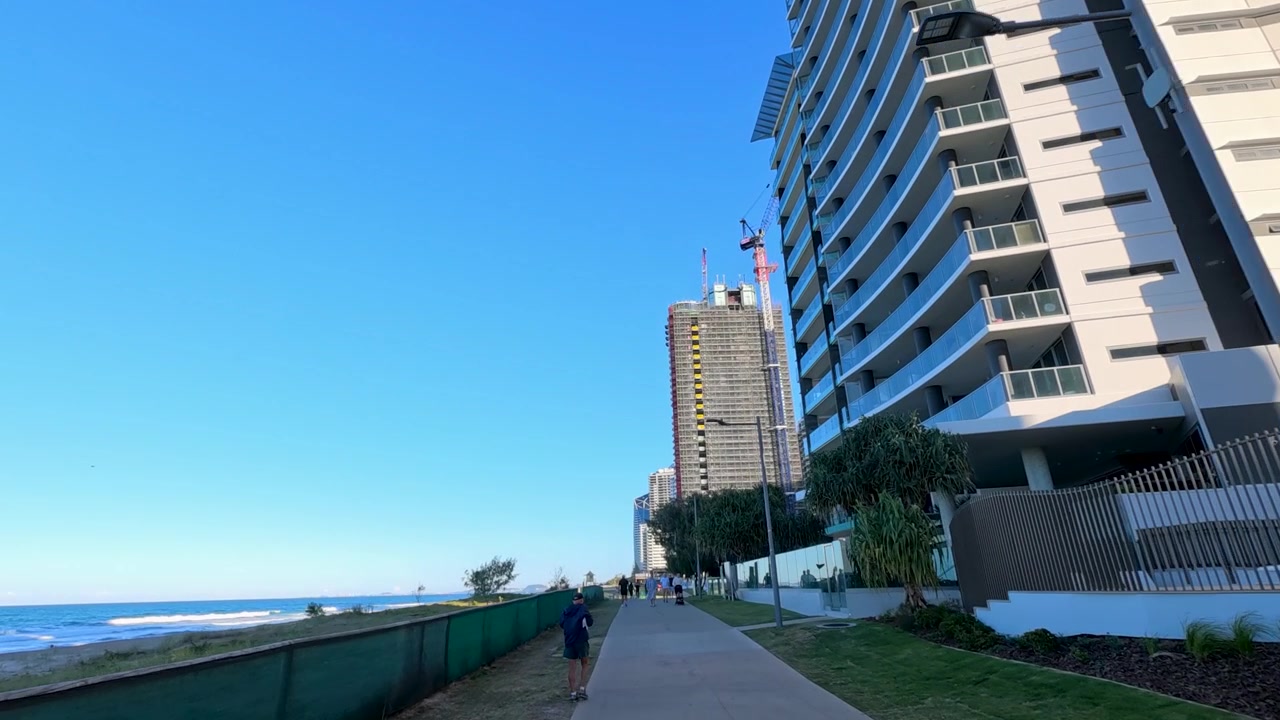 Persone camminano lungo un sentiero costiero accanto a moderni grattacieli e all'oceano a Surfers Paradise