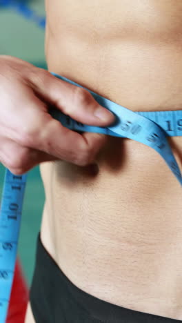 close up mid section of a shirtless fit swimmer measuring waist