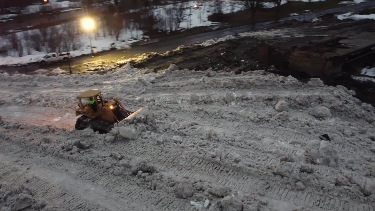 бульдозер выталкивает огромную кучу снега со снежной свалки