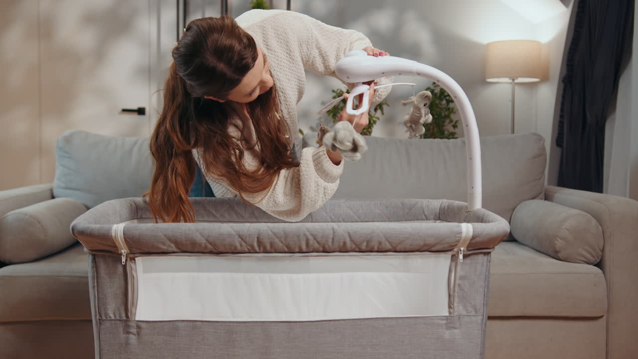 Pregnant woman assembling baby crib with mobile in nursery room preparing for newborn arrival