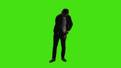 man putting on wireless headphones and streaming music from mobile phone against green screen with low key lighting 1