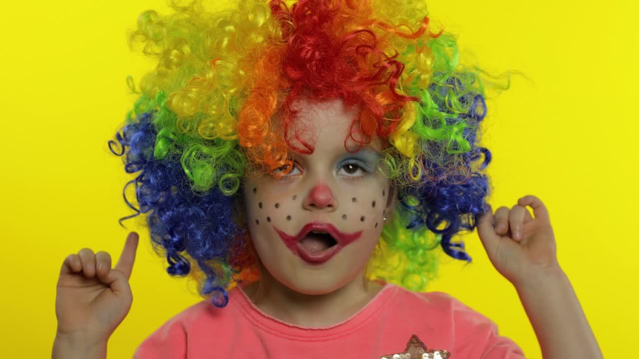 una niña payasa con una peluca colorida haciendo caras tontas. divirtiéndose, sonriendo, bailando. halloween