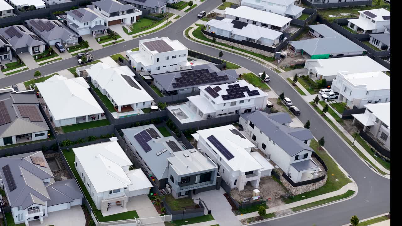 Drone camera glides above contemporary suburban homes, revealing curving streets and lush forest backdrop