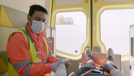 paramedic wearing facial mask touching the hand of a patient lying on the stretcher inside an ambulance