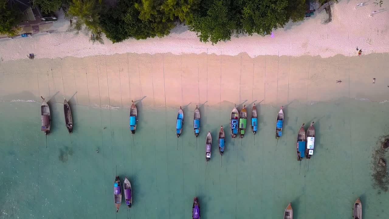 4k aéreo arriba moviéndose hacia abajo toma de botes largos amarrados en la playa en la bahía de la isla phi phi, phi phi don, tailandia