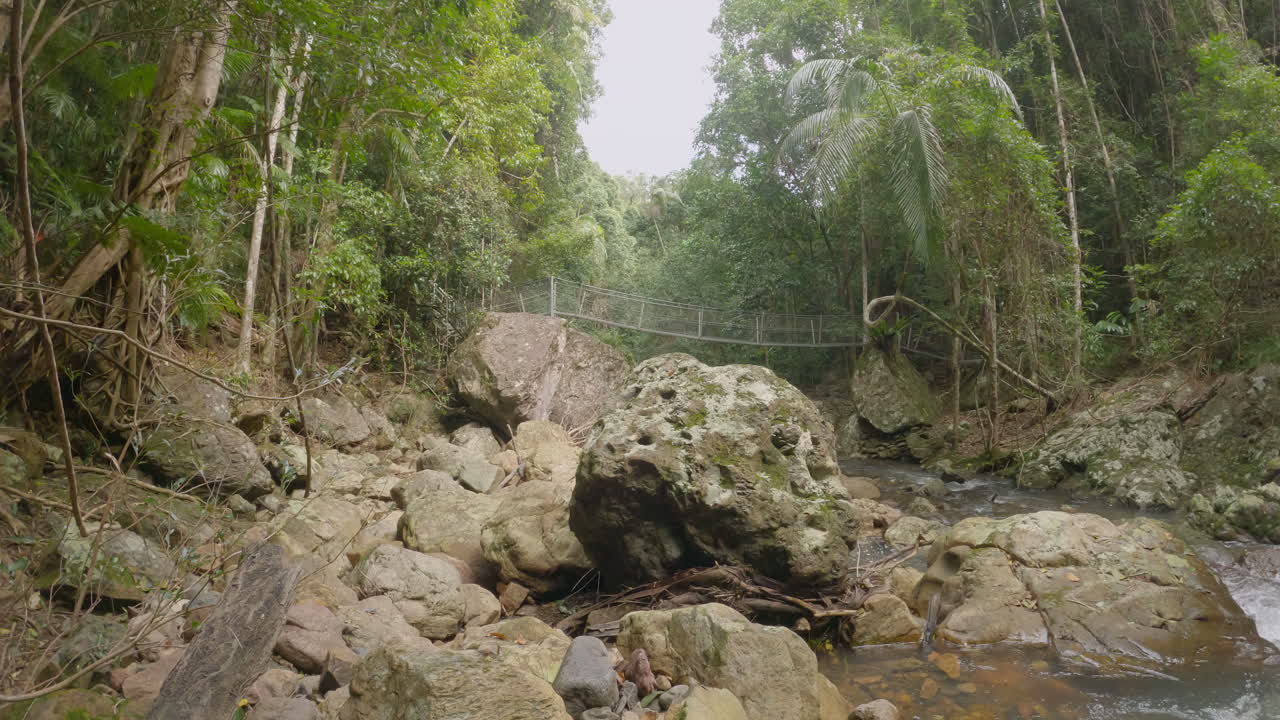 el hombre camina sobre el puente colgante en la distancia sobre el arroyo baxter que fluye rápidamente