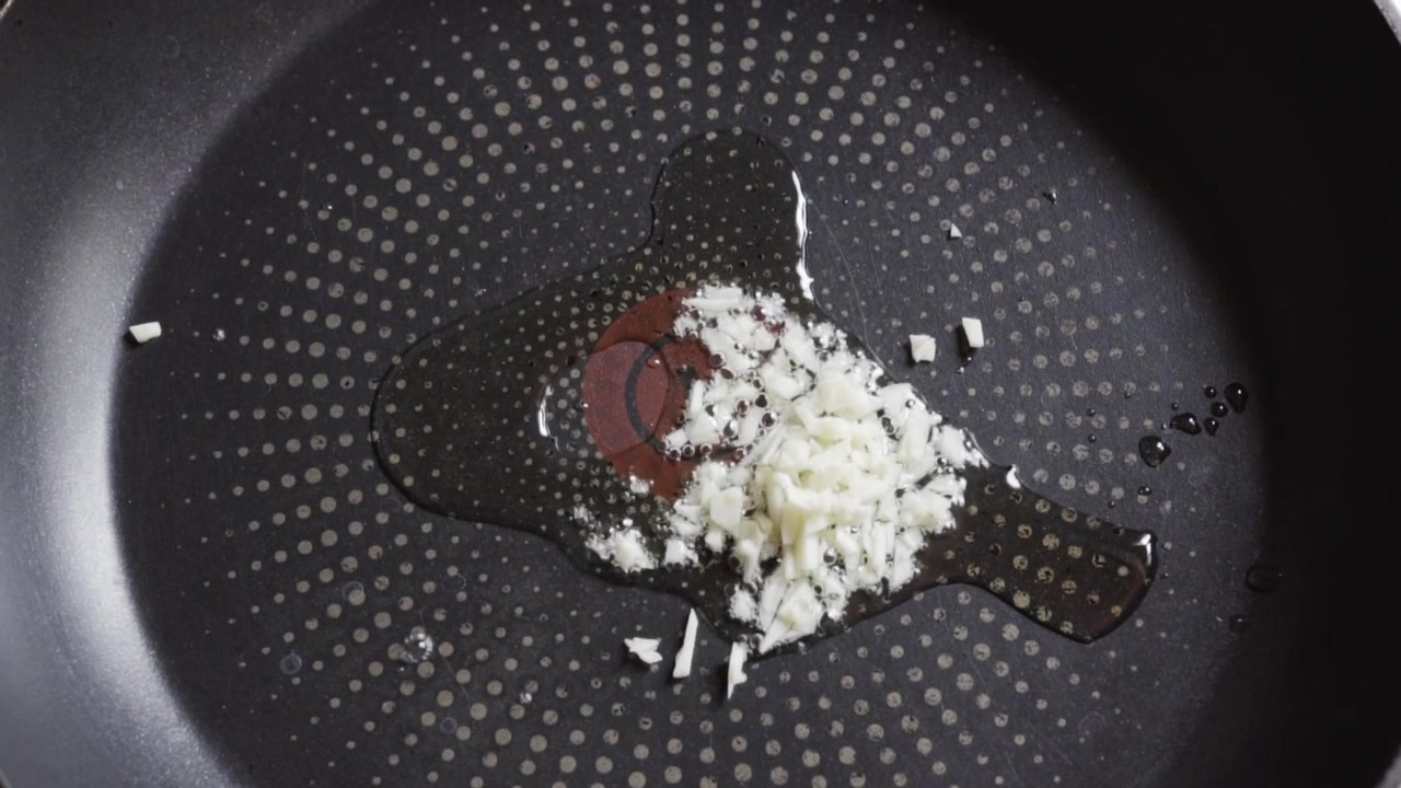 Chopped garlic added to hot oil in nonstick pan , close up top view, handheld kitchen shot