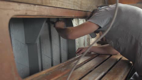 young man painting interior of wooden boat with aluminium wood primer