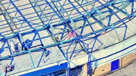 drone footage highlights the blue steel roof structure of st andrew’s stadium, featuring a prominently waving usa flag among the beams on a bright, sunny day