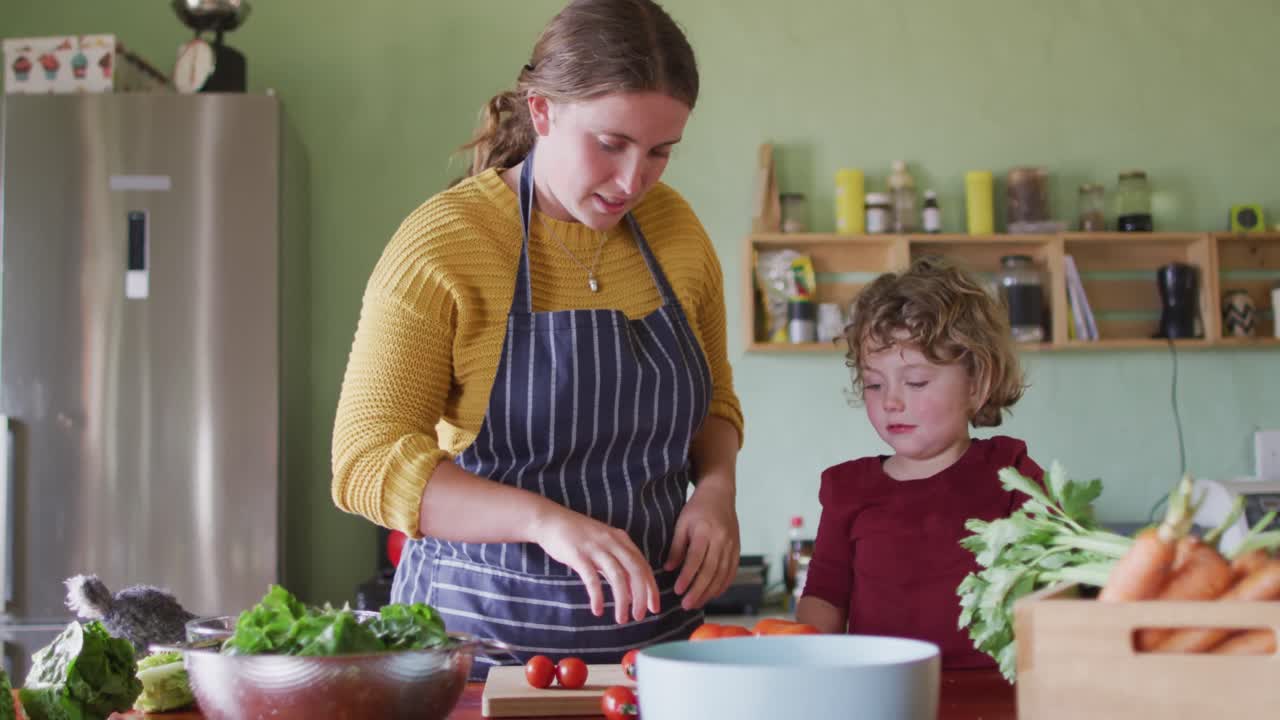madre y hijo caucásicos felices cortando verduras en la cocina