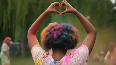 person making heart hands at a colorful holi festival