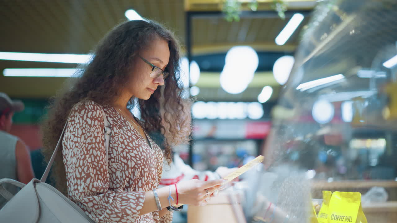 Side view of a woman in vintage attire standing thoughtfully in front of a store, holding an item with contemplation, soft bokeh lights create a warm atmosphere as another person stands nearby