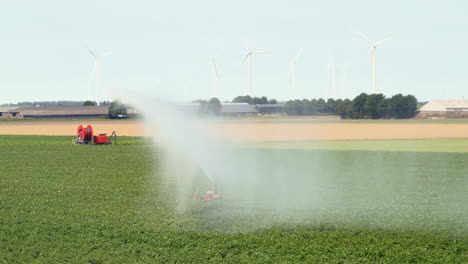 sistema de riego agrícola rociando agua sobre cultivos, aerogeneradores en segundo plano, cámara lenta-2