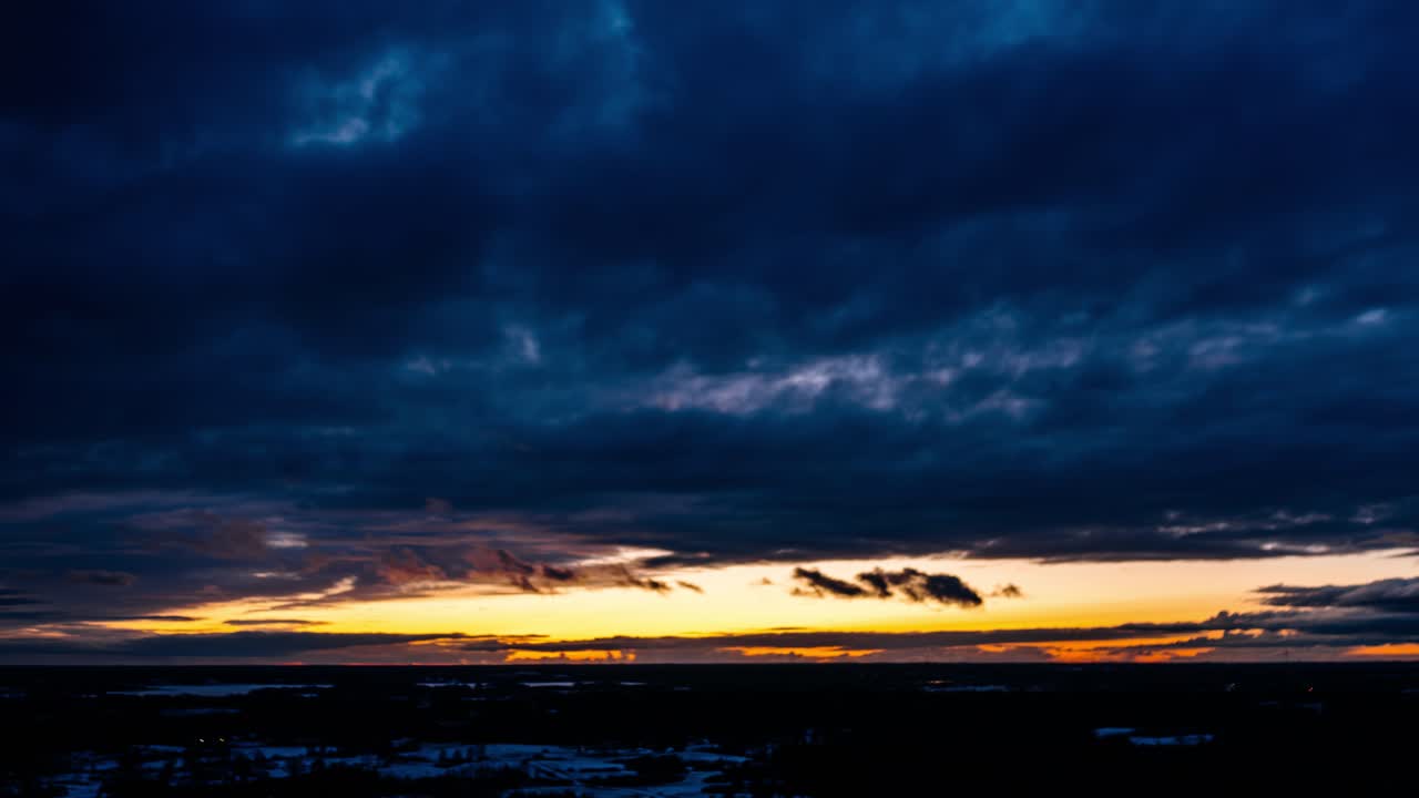 Aerial winter hyperlapse with dark clouds covering evening sunlight. Sunset behind clouds up in the air. Wide drone view of cloudscape in countryside.