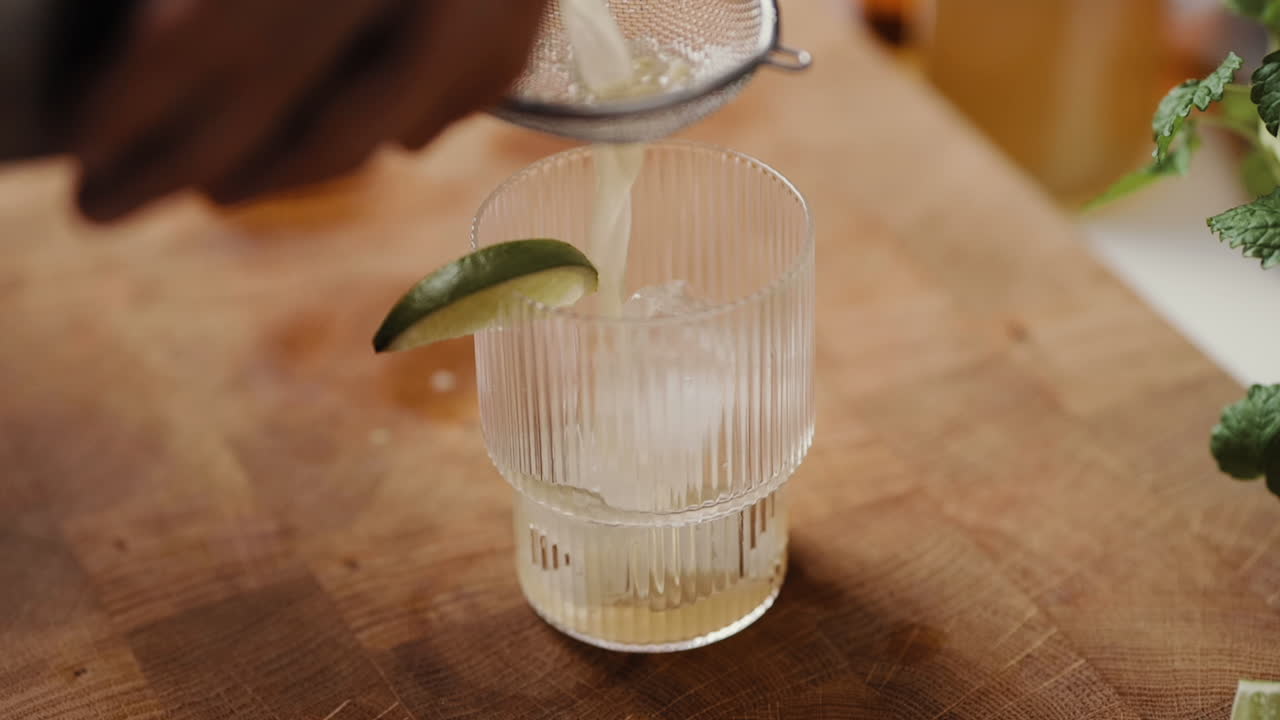 macho joven vertiendo un cóctel a través de un tamiz en un vaso en la cocina de casa