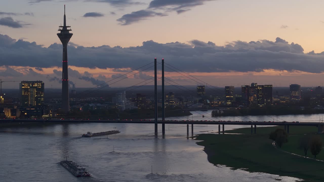 Pramme sejler på den oversvømmede Rhinflod gennem Düsseldorf i skumringen, tele-droneoptagelse