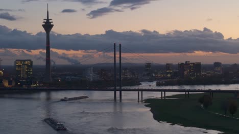 barcazas navegan en el inundado río rin a través de dusseldorf al anochecer, telefoto tomada por un dron