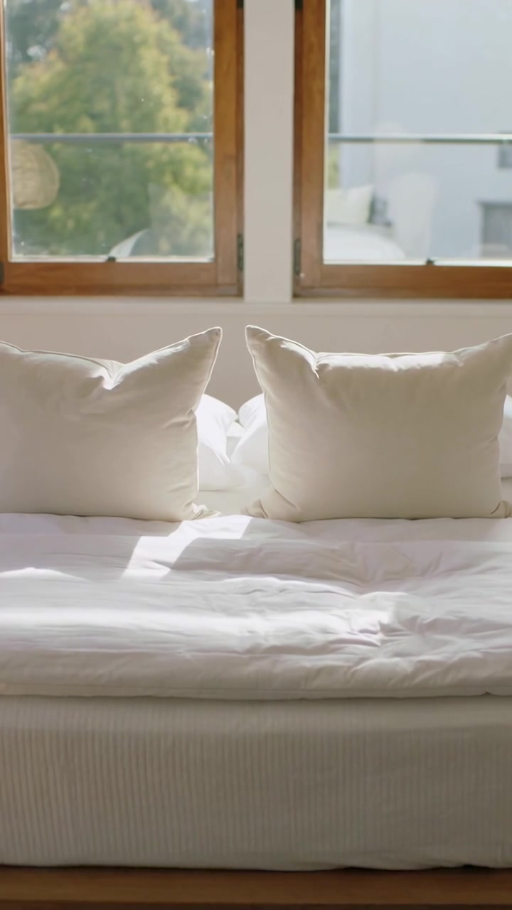 Video verticale: Donna in top bianco che entra e sistema il materasso di un divano letto vicino a finestre di legno, spazio per il testo.