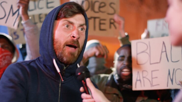 Close-up view of a caucasian man agitatedly answering interviewer's questions in a manifestation against racism with group of multi-ethnic people