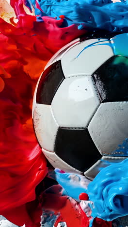 a soccer ball is in the middle of a colorful explosion of paint. the ball is surrounded by a mix of red, blue, and yellow colors, creating a dynamic and energetic scene