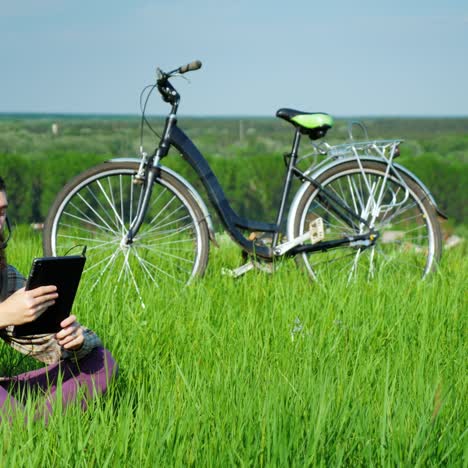 a young bearded man talks via video link sitting near a bicycle in a green meadow