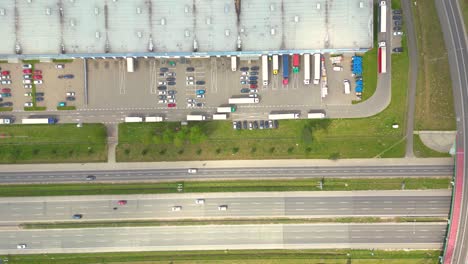 logistics park with warehouse, loading hub and many semi trucks with cargo trailers standing at the ramps for load unload goods at sunset