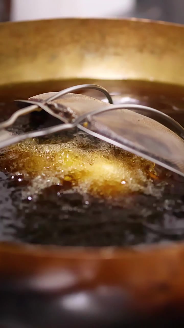 Close-up of samosas deep frying in hot oil within a brass wok in Bangkok.