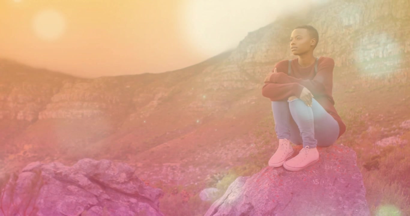 Woman crouching on boulder as rising sun creating animated light flares over canyon for wellness