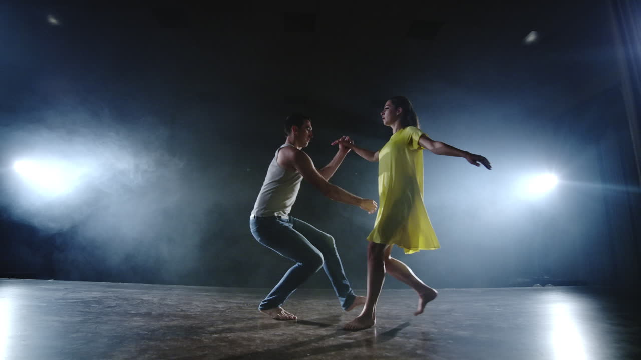 Dramatic spins and flips of a modern ballet dancer from a musical. A single woman emotionally dances on stage against a dark background with smoke in the spotlight in slow motion.