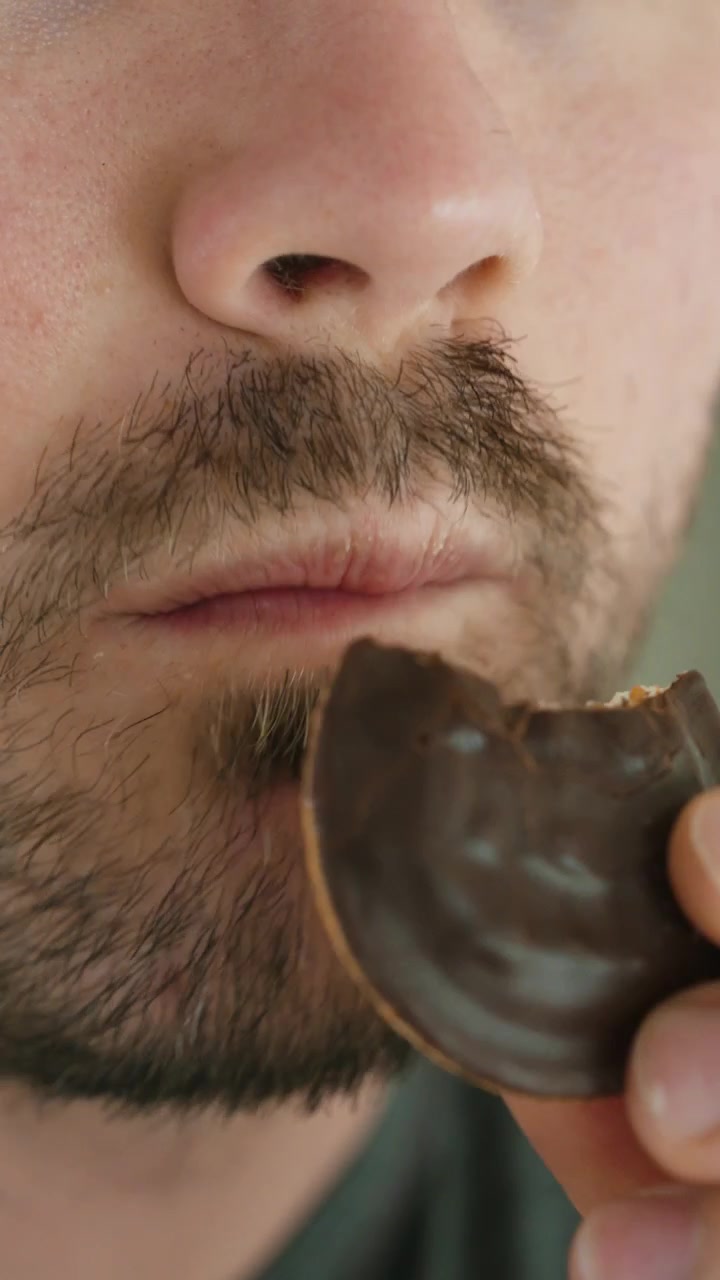 Close-up shot of a man eating a chocolate cookie, representing sugar cravings, unhealthy snacks, sweet food, obesity risk, diabetes awareness, diet choices, and modern eating habits.
