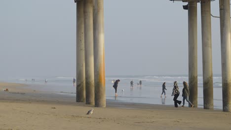 Dos-Chicas-Caminando-Bajo-El-Muelle-En-Huntington-Beach,-California