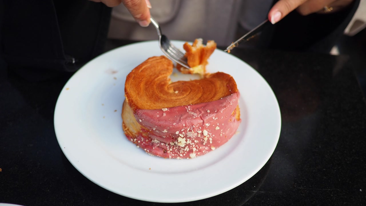 Person Cutting a Delicious Pink Glazed Pastry with Fork and Knife