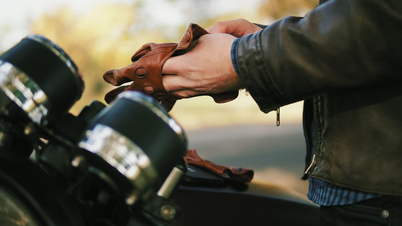vista lateral de y motociclista irreconocible tomando guantes de cuero marrón y el uso de guantes de cuero especiales para conducir en lento