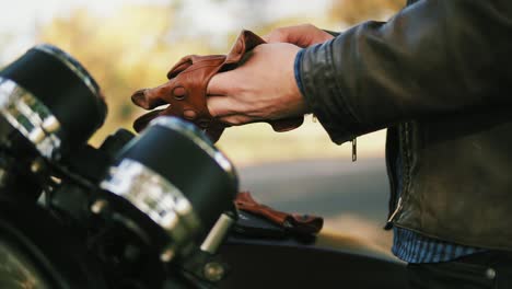 Side-view-of-and-unrecognizable-motorcyclist-taking-brown-leather-gloves-and-wearing-special-leather-mitts-for-riding-in-slow