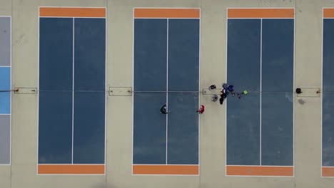 A-top-down-view-high-over-several-pickle-ball-courts-with-four-players-congratulating-each-other-after-a-game-on-a-cloudy-day
