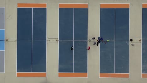 a top down view high over several pickle ball courts with four players congratulating each other after a game on a cloudy day