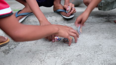 Kids-Wearing-Slippers-Playing-Happily-Pogs-Or-Milk-Caps-On-Ground