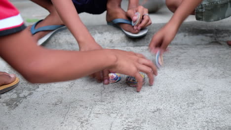 kids wearing slippers playing happily pogs or milk caps on ground