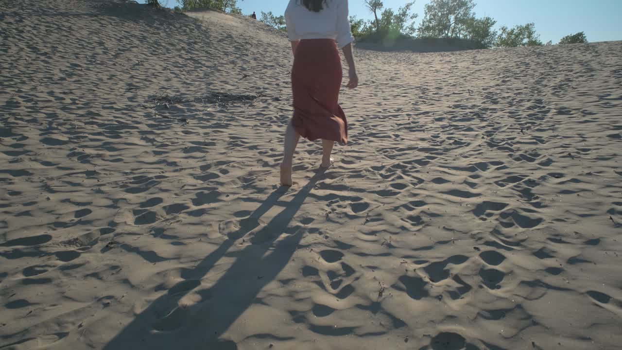 Camera following the footsteps of a woman walking barefoot in the sand dunes of Sandbanks