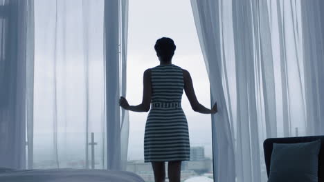 happy young woman opening curtains looking out window ready for fresh new day feeling rested enjoying view of city