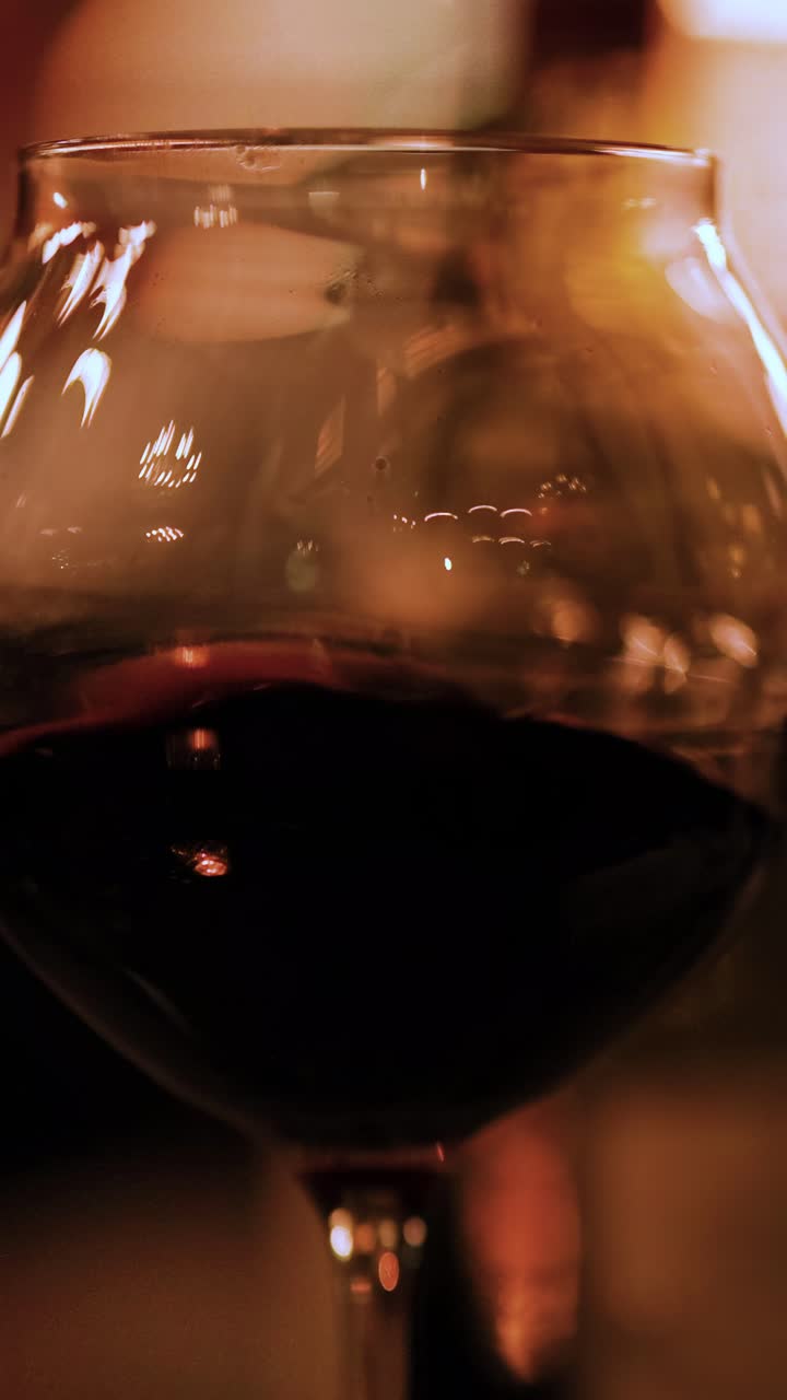 Un primo piano di un calice di vino rosso, su uno sfondo caldo e illuminato da luce soffusa, che crea un'atmosfera accogliente.