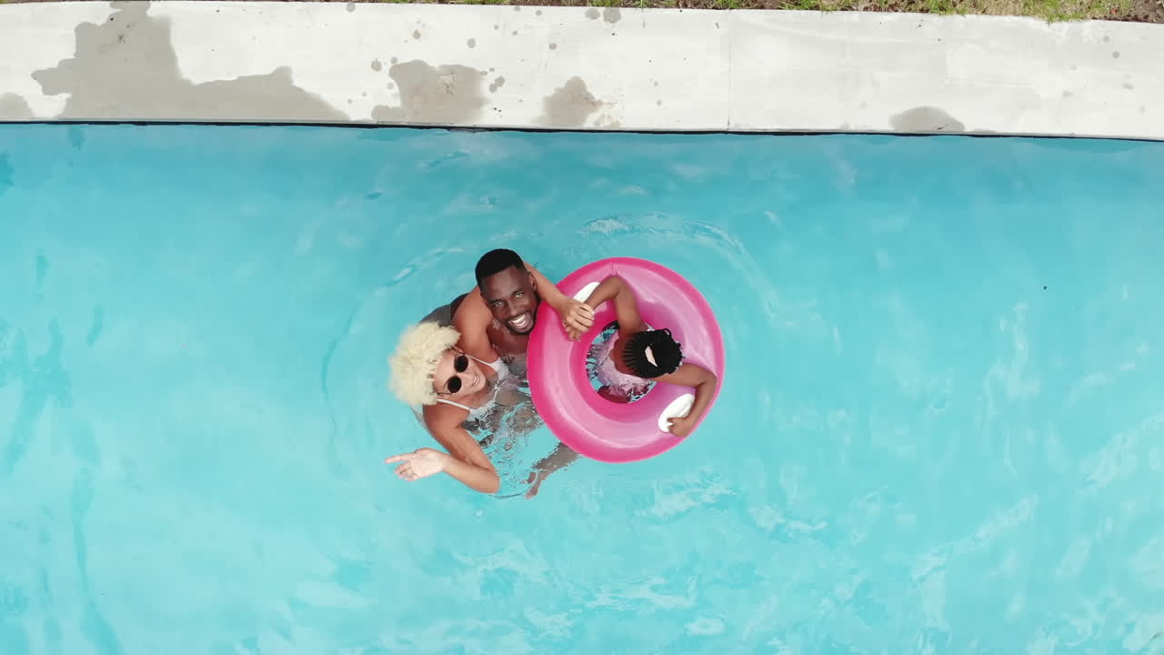An African American family floats on a pink inflatable ring in a pool at home