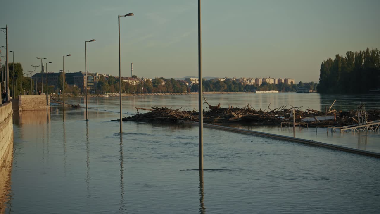 Flooded riverside with submerged streetlights and large debris piles floating on the water, Budapest, Hungary